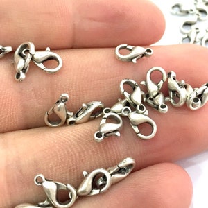 May include: A close-up of a pile of silver-toned lobster claw clasps. The clasps are small and delicate, and they are perfect for adding a touch of elegance to jewellery.