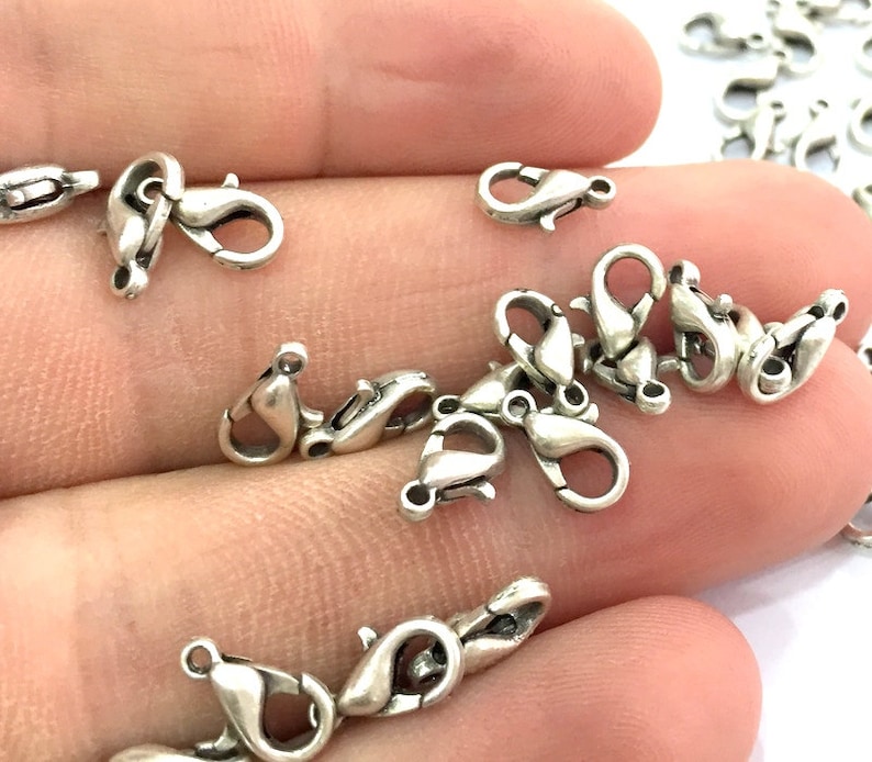 May include: A close-up of a pile of silver-toned lobster claw clasps. The clasps are small and delicate, and they are perfect for adding a touch of elegance to jewellery.