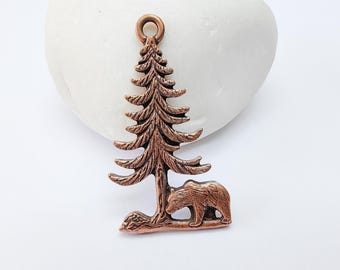 May include: A copper charm featuring a detailed pine tree with a bear standing beneath it. The charm has a loop at the top for hanging.