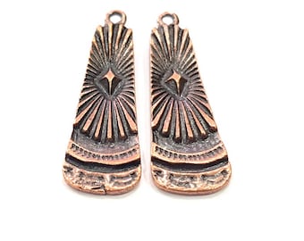 May include: A pair of copper-toned earring findings with a geometric design. The findings have a starburst pattern and a diamond-shaped center.