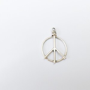 May include: A silver peace sign charm pendant. The charm is a circle with a peace sign inside.