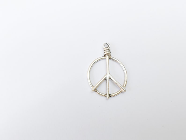 May include: A silver peace sign charm pendant. The charm is a circle with a peace sign inside.
