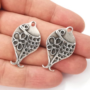 May include: Two silver-toned metal charms shaped like fish with a floral design. The charms have a loop at the top for attaching to jewelry or other crafts.