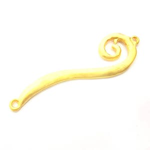 May include: A gold-colored metal bookmark with a decorative swirl at the top. The bookmark is curved and has a smooth, brushed finish.