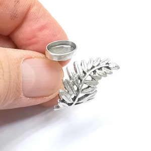 May include: Silver fern charm with a round, silver-toned bezel setting. The charm is designed to hold a small cabochon.