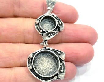 Op de afbeelding: Zilveren hanger met twee ronde, open, ronde frames. De frames zijn met elkaar verbonden door een ketting en hebben een getextureerd, versierd ontwerp.