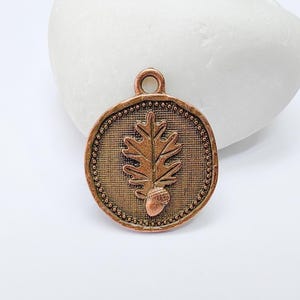 Peut inclure: Pendentif rond de couleur cuivrée avec un motif de feuille de chêne et de gland. Le pendentif a un fond texturé et une bordure perlée. Il comporte une petite boucle en haut pour la suspension. Idéal pour la fabrication de bijoux ou l'artisanat.