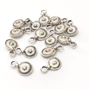 Puede incluir: Un grupo de dijes de metal plateado con un diseño floral decorativo. Cada dije tiene un bucle para sujetarlo a un collar, pulsera u otras joyas.