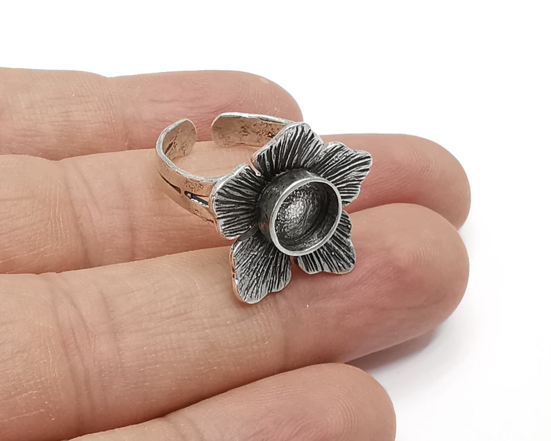 Op de afbeelding: Zilveren ring met een bloemmotief. De bloem heeft een rond, open midden dat kan worden gebruikt om een klein voorwerp te houden, zoals een steen of een bedel.