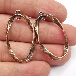 Puede incluir: Dos aros ovalados de cobre con un diseño retorcido. Los aros tienen un acabado liso y martillado.