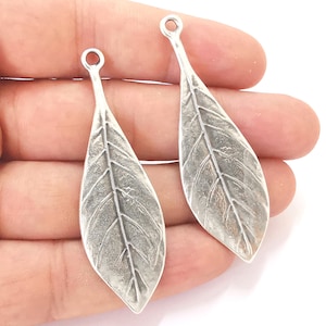 Peut inclure: Deux pendentifs argentés en forme de feuille. Chaque pendentif présente un motif de veines de feuilles détaillé et une petite boucle en haut pour l'accrochage. Les pendentifs sont en métal avec un aspect légèrement vieilli, suggérant un style vintage ou artisanal.