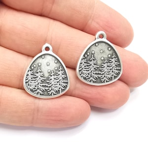 May include: Two silver-toned metal charms shaped like a triangle with a forest scene and a crescent moon with stars. The charms have a loop at the top for attaching to jewelry.
