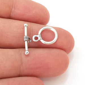 Puede incluir: Cierre de palanca de plata con un anillo redondo. El cierre está hecho de metal y tiene un acabado pulido.