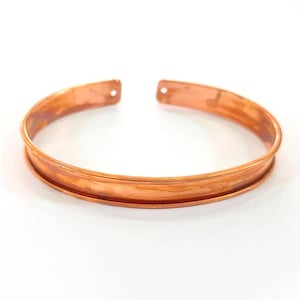 May include: A copper bracelet with a hammered finish and a slightly rounded shape.