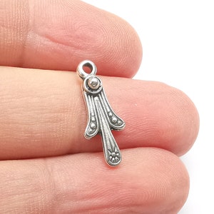 May include: Silver charm with a decorative design resembling a stylized leaf or flower. The charm has a small loop at the top for attaching to jewelry or other crafts.