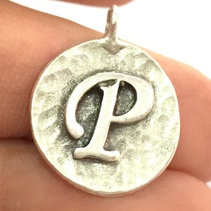 Puede incluir: Encanto de plata con acabado martillado y la letra P en fuente cursiva.