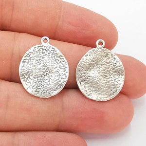 May include: Two silver-toned metal circle charms with a textured surface and a loop for hanging.