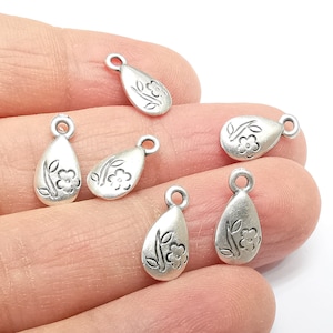 Peut inclure: Six breloques en argent en forme de goutte avec un motif floral. Chaque breloque a une petite boucle en haut pour l'attacher à des bijoux ou d'autres objets artisanaux.