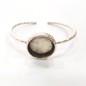 Könnte beinhalten: Silbernes Armreif-Armband mit einer runden, gehämmerten Metallfassung. Die Fassung ist für einen runden Cabochon ausgelegt.