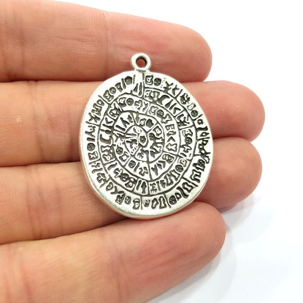 May include: Silver pendant with a circular design featuring a circular pattern of symbols and letters. The pendant has a loop at the top for attaching to a chain.