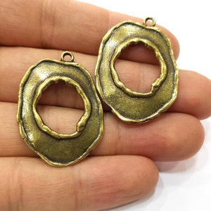 Peut inclure: Deux pendentifs antiques de couleur laiton avec un design organique en couches. Chaque pendentif présente une ouverture circulaire centrale et une petite boucle en haut pour l'attacher à une chaîne ou à un autre composant de bijou. Les pendentifs ont une surface texturée.