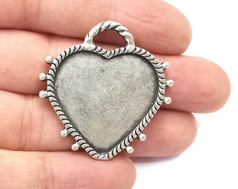 May include: Silver heart-shaped pendant with a rope-like border and small beads around the edge. The pendant has a loop at the top for attaching a chain.
