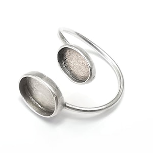 May include: A silver ring with two oval-shaped settings. The ring is open and has a curved design.