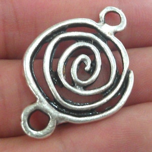 Puede incluir: Encanto de metal plateado con un lazo doble para sujetar a las joyas. El encanto presenta un diseño en espiral detallado.