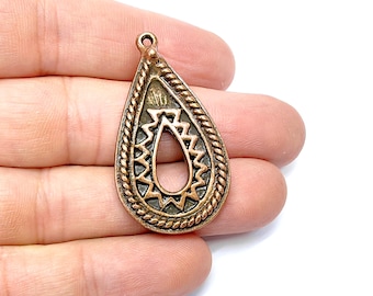 May include: A copper-colored teardrop-shaped pendant with a decorative design. The pendant has a hole in the center for stringing.