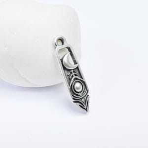 Puede incluir: Encanto de plata con una luna creciente, un círculo y un diseño de pluma estilizado.