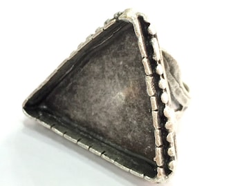 May include: Silver triangular ring with a decorative border. The ring is designed to hold a cabochon stone.