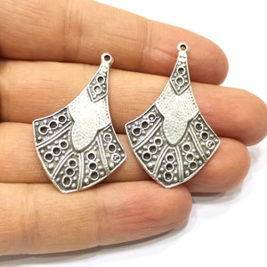 May include: Two silver-toned metal earring charms with a geometric design. The charms have a textured surface and a loop at the top for attaching to earrings.