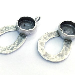 Puede incluir: Dos ajustes de colgante de plata con un diseño ovalado martillado y un bisel redondo para una piedra de cabujón.