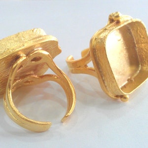 Puede incluir: Dos anillos de tono dorado con engastes cuadrados para piedras cabujón. Los anillos son ajustables y tienen un acabado texturizado.