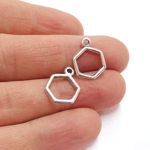 May include: Two silver hexagon shaped charms with a loop at the top. The charms are open and have a smooth, shiny finish.
