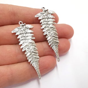 May include: Two silver fern leaf charms with a textured surface. The charms have a loop at the top for attaching to jewelry or other crafts.