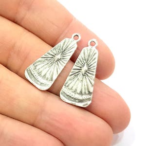 Puede incluir: Un par de charms para pendientes de color plateado con un diseño de estrella y un pequeño acento en forma de diamante en el centro.