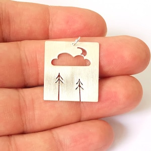 Puede incluir: Encanto de colgante de plata con un diseño recortado de una nube, una luna y dos pinos. El encanto es rectangular y tiene un acabado de plata cepillada.