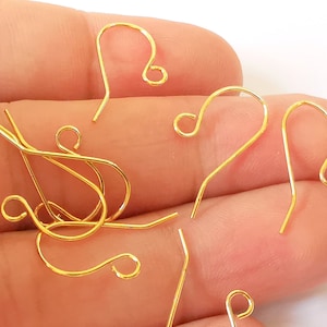 May include: A close-up of a group of gold-colored earring hooks. The hooks are made of metal and have a simple, elegant design.