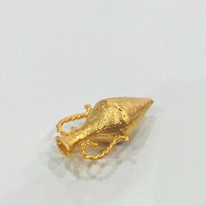 May include: A gold-colored metal pendant in the shape of a small, ornate vase with a pointed top.