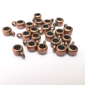 May include: A group of 18 copper-toned metal end caps for jewellery making. The end caps have a round shape with a small loop on one side.