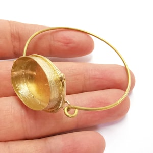 May include: A gold-toned bangle bracelet with a hinged, oval-shaped locket. The locket is open and the inside is visible.