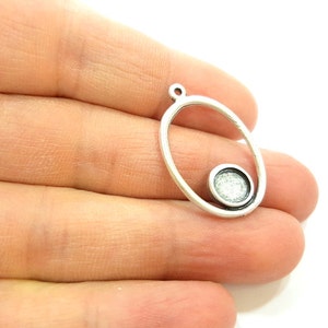 May include: Silver oval pendant with a smaller circle inside. The circle has a textured surface.