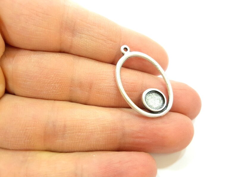 May include: Silver oval pendant with a smaller circle inside. The circle has a textured surface.