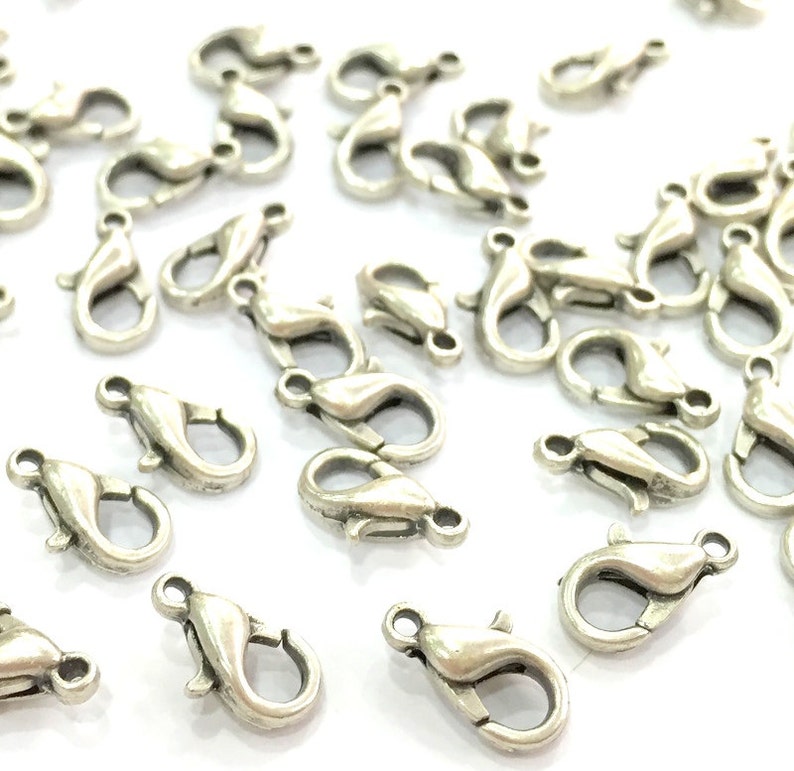 May include: A pile of silver-toned lobster claw clasps, a type of jewellery finding used for attaching chains or cords to necklaces, bracelets, and other jewellery.