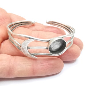 Peut inclure: Bracelet manchette argenté avec une lune en croissant et un sertissage rond. Le bracelet présente un design à trois bandes. La lune a une texture martelée. Le design ouvert permet un port facile. Un bijou sur le thème céleste.