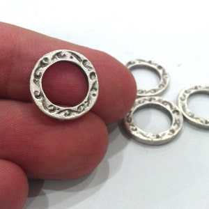 May include: Five silver-toned metal rings with an ornate design. The rings are approximately 1 inch in diameter.