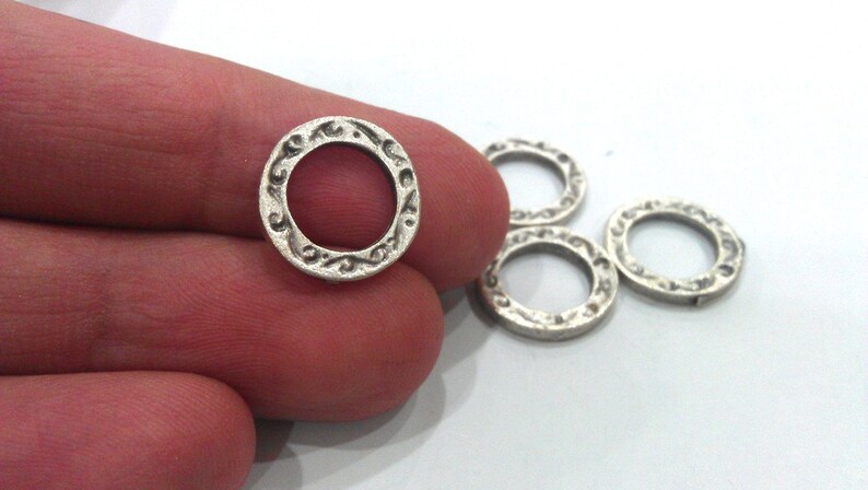 May include: Five silver-toned metal rings with an ornate design. The rings are approximately 1 inch in diameter.