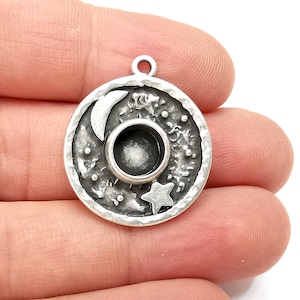 May include: Silver charm with a round design featuring a crescent moon, a star, and a small circle in the center. The charm has a textured surface and a loop for attaching to a necklace or bracelet.