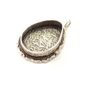 Könnte beinhalten: Silberner Anhänger mit einem dekorativen, verzierten Design auf der Rückseite. Der Anhänger ist oval geformt und hat eine Öse zum Anbringen einer Kette.